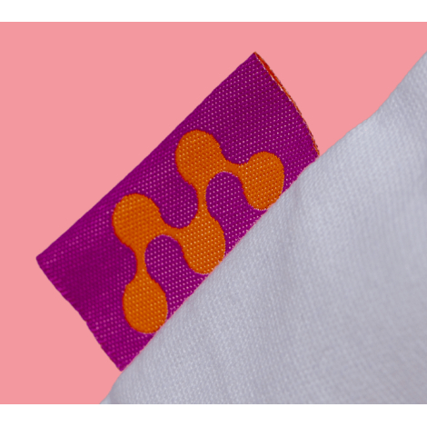 Gros plan sur l’étiquette tissée latérale du tote bag, montrant un motif coloré sur textile, aucune personnalisation apparente.