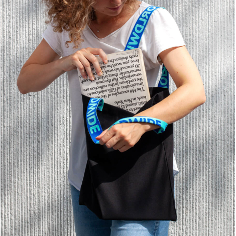 Tote bag noir vu de trois-quarts, anses jacquard posées sur l’épaule et la poitrine, ouverture principale visible, sans marquage