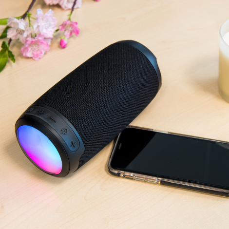 Enceinte noire éclairée en dégradé coloré posée près d’un smartphone
