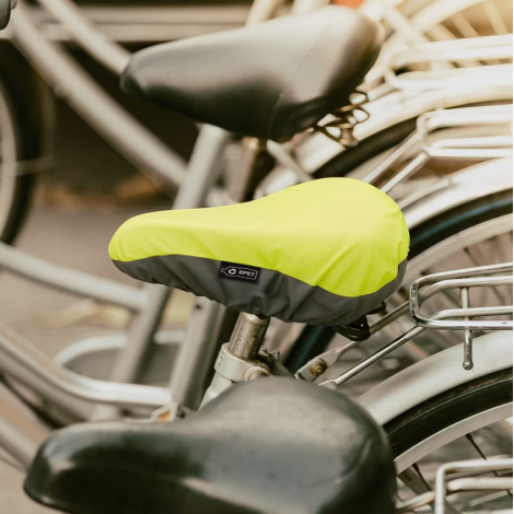 Housse de selle en R-PET installée sur une selle de vélo en extérieur, zone réfléchissante identifiable, sans marquage visible.