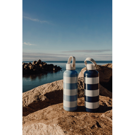 Deux bouteilles isothermes en acier inoxydable présentées debout en extérieur sur des rochers face à un plan d’eau, motif rayé b