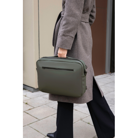 Sac ordinateur porté à la main par une femme en environnement urbain, modèle vert foncé avec poignée supérieure et poche zippée 
