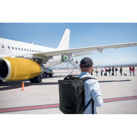 Sac de voyage cabine porté sur le dos par un homme sur un tarmac d’aéroport face à un avion, sans marquage visible sur le sac