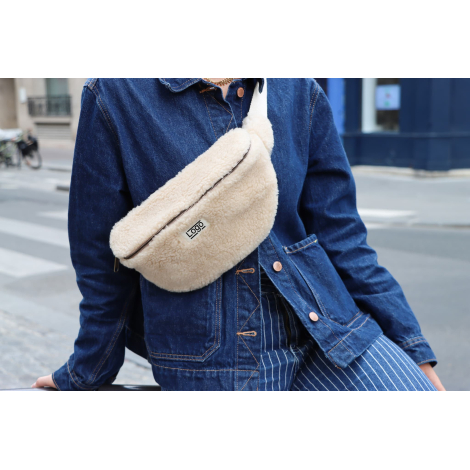 Banane effet moumoute écrue portée en bandoulière avec étiquette personnalisée visible.