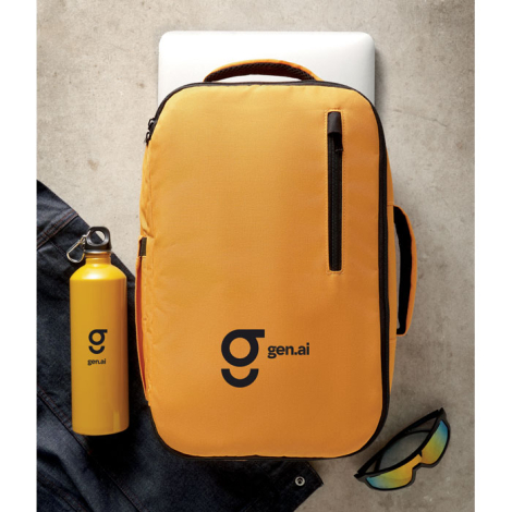 Sac à dos cabine présenté en situation au sol, vue de face, avec accessoires autour et une personnalisation visible sur la face 