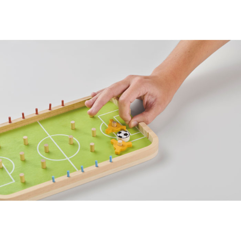 Jeu de football en bois en situation sur fond clair, main manipulant une pièce sur le plateau avec surface de jeu et éléments mo