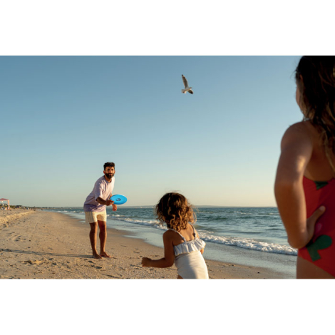 Frisbee utilisé en situation de jeu sur une plage, visible à distance entre des personnes en extérieur, sans personnalisation cl