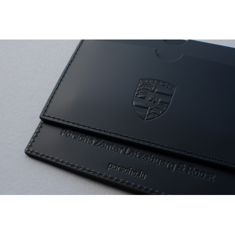 Gros plan sur un étui carte grise en cuir foncé montrant les coutures et une personnalisation embossée visible.
