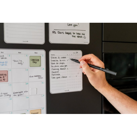 Plusieurs suivis d’habitudes adhésifs fixés sur une surface verticale, dont un en cours d’écriture avec inscriptions visibles.