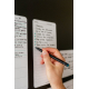 Plusieurs listes de tâches adhésives fixées sur une surface verticale, dont une en cours d’écriture avec inscriptions visibles.