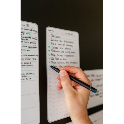 Plusieurs listes de tâches adhésives fixées sur une surface verticale, dont une en cours d’écriture avec inscriptions visibles.