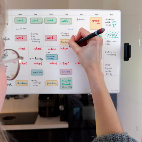 Calendrier hebdomadaire adhésif fixé sur une surface verticale claire, avec grille hebdomadaire et inscriptions manuscrites visi