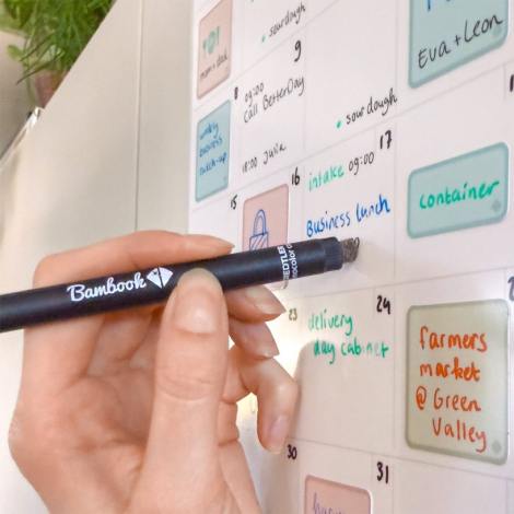 Planificateur mensuel adhésif fixé sur une surface verticale, avec écriture manuscrite visible sur la grille.