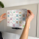 Planificateur mensuel adhésif partiellement décollé d’une surface verticale, avec inscriptions visibles.