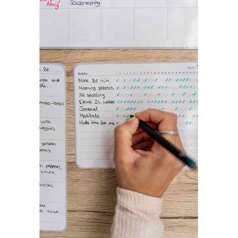 Suivi d’habitudes mensuel adhésif en situation d’écriture, avec main tenant un stylo et marquage visible sur la surface.