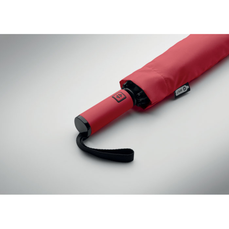 Gros plan sur la poignée d’un parapluie plié rouge avec dragonne noire, présenté sur fond clair, sans personnalisation visible.