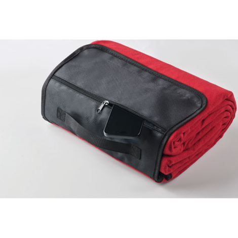 Couverture rouge roulée maintenue par rabat noir avec poche zippée, présentée en perspective, sans marquage visible.