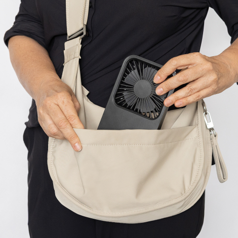Ventilateur glissé dans un sac porté en bandoulière, tenu par une personne, sans marquage apparent.