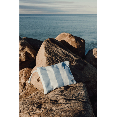 Pochette posée sur des rochers en bord de mer, présentée en situation d’usage, sans personnalisation apparente.