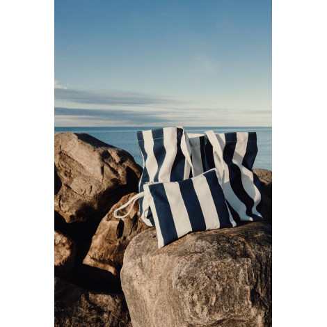 Pochette présentée avec un sac de plage assorti sur des rochers, illustrant un ensemble coordonné, sans marquage visible.