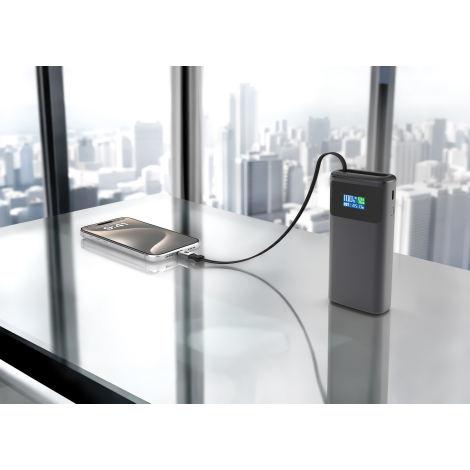 Batterie externe posée sur une surface vitrée connectée à un smartphone avec vue urbaine en arrière-plan, sans marquage visible.