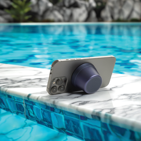 Haut-parleur fixé à l’arrière d’un smartphone posé au bord d’une piscine, en situation extérieure, sans marquage visible.