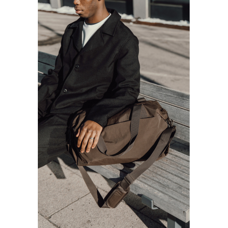 Sac posé à côté d’une personne assise sur un banc, présenté en situation d’usage, sans marquage apparent.