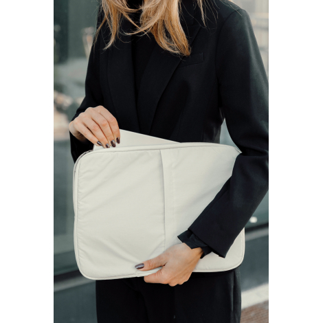 Housse beige tenue par une femme lors de l’insertion d’un ordinateur, en situation d’usage, sans personnalisation visible.