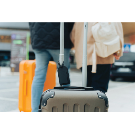 Étiquette fixée sur une valise en déplacement avec des personnes en arrière-plan, présentée en situation réelle, sans marquage a