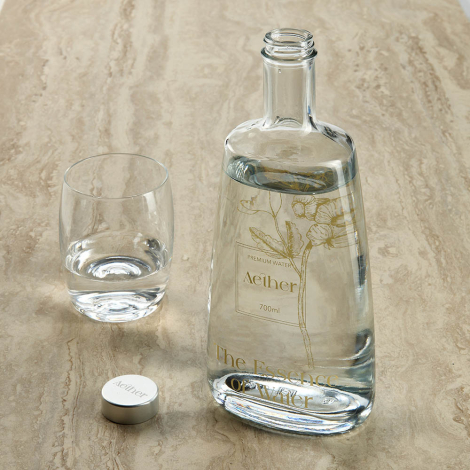 Bouteille en verre remplie avec un verre à côté et bouchon posé au sol, avec marquage visible sur la surface extérieure