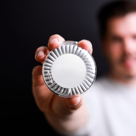 Boîtier rond blanc tenu en main par un homme, surface extérieure visible sans marquage