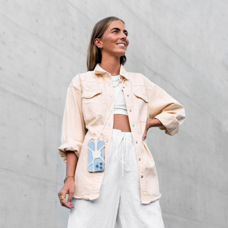 Smartphone porté en bandoulière par une femme avec système de fixation visible au dos de la coque, sans marquage apparent