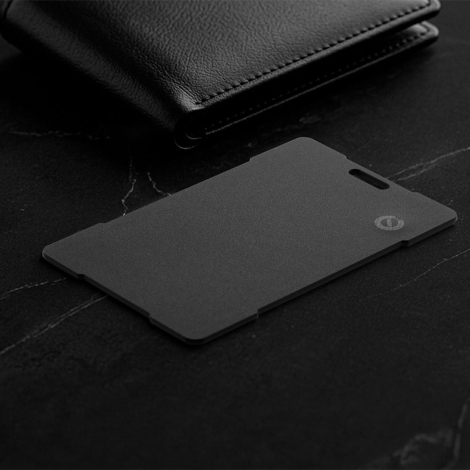 Traceur noir format carte posé à côté d’un portefeuille sur surface sombre, sans personnalisation visible