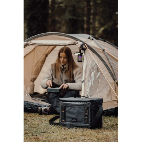 Personne assise devant une tente avec sac isotherme posé à côté sans marquage visible