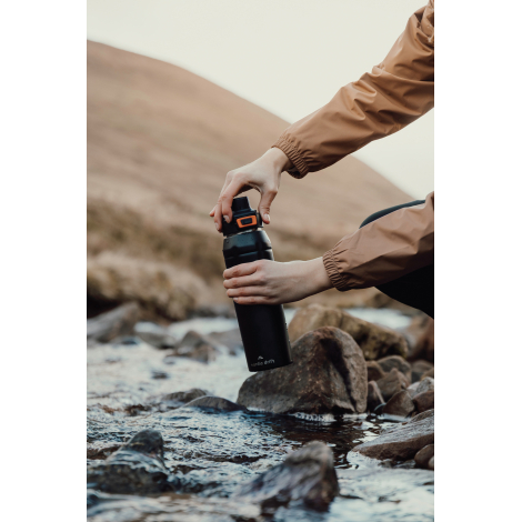 Personne utilisant une bouteille en extérieur près d’un cours d’eau, sans personnalisation visible