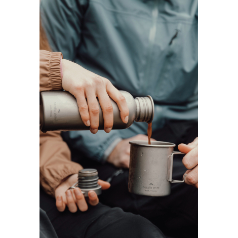 Personne versant une boisson depuis la gourde dans une tasse, sans personnalisation visible