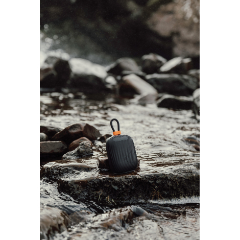 Enceinte posée sur des pierres en extérieur avec eau en arrière-plan sans marquage visible