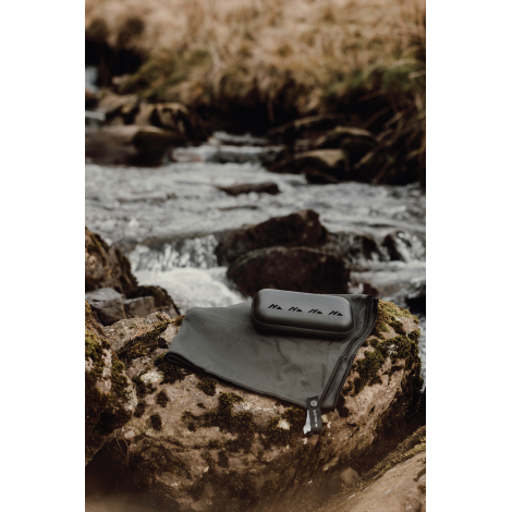 Serviette microfibre déployée au sol avec étui posé dessus en extérieur sans marquage visible