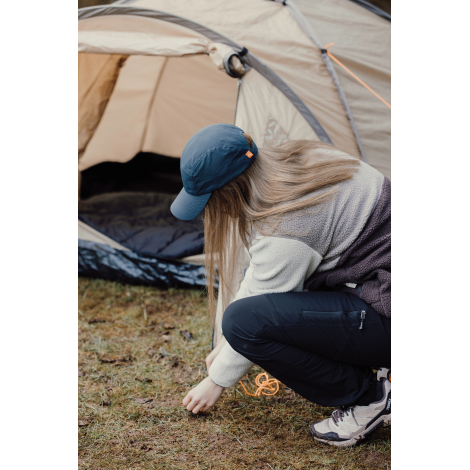 Casquette bleue portée par une femme accroupie en extérieur près d’une tente sans marquage visible