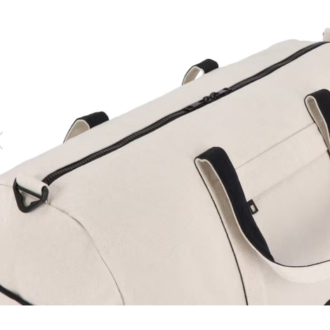 Vue rapprochée du dessus d’un sac de voyage beige avec fermeture zippée noire et poignées visibles, sans marquage apparent.