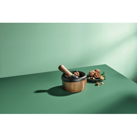 Ensemble mortier et pilon présenté sur une table avec des cerneaux de noix et des feuilles fraîches, sans personnalisation appar