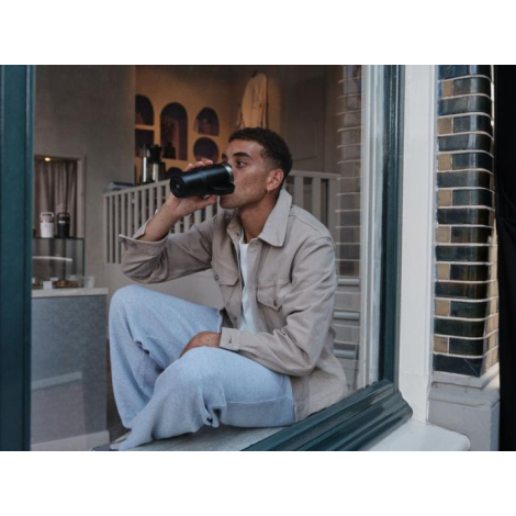 Homme assis utilisant un mug isotherme noir, aucune personnalisation visible sur la face présentée.