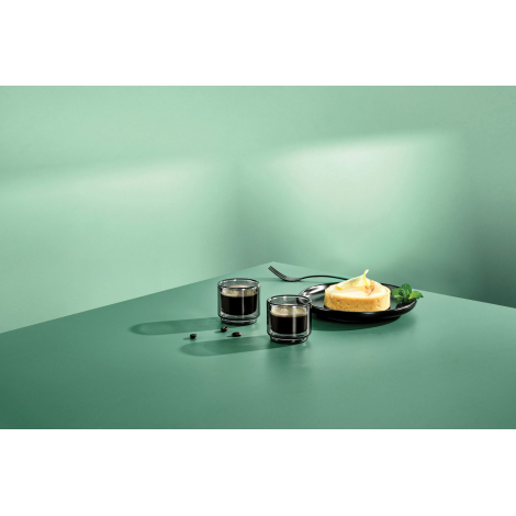 Deux tasses à expresso en verre double paroi présentées en situation d'utilisation sur une table avec une part de dessert.