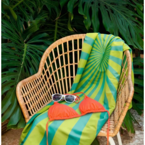 Serviette de plage imprimée disposée sur un fauteuil en rotin avec des accessoires de plage.