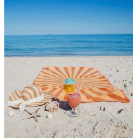 Serviette de plage imprimée déployée sur le sable avec des accessoires de plage.