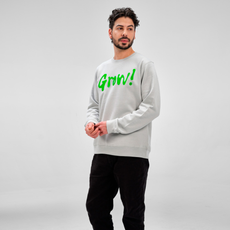 Homme portant un sweat unisexe gris clair dans un studio photo, avec un marquage visible sur la poitrine côté gauche.