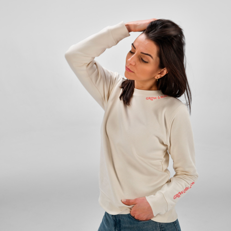 Femme portant un sweat femme à col rond écru avec un marquage visible au niveau du col sur la face avant et sur le bas de la man