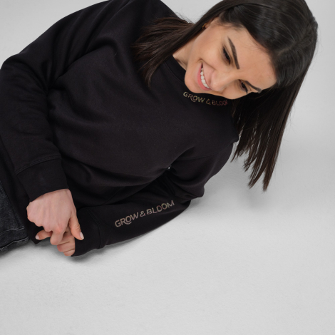 Femme portant un sweat femme à col rond noir avec un marquage visible au niveau du col sur la face avant et sur le bas de la man
