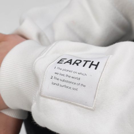 Gros plan sur la manche d'un sweat unisexe blanc à col montant zippé avec une étiquette textile cousue visible près du poignet.