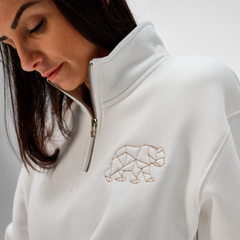 Gros plan sur une femme portant un sweat unisexe blanc à col montant avec demi-fermeture zippée. Une broderie est visible sur la